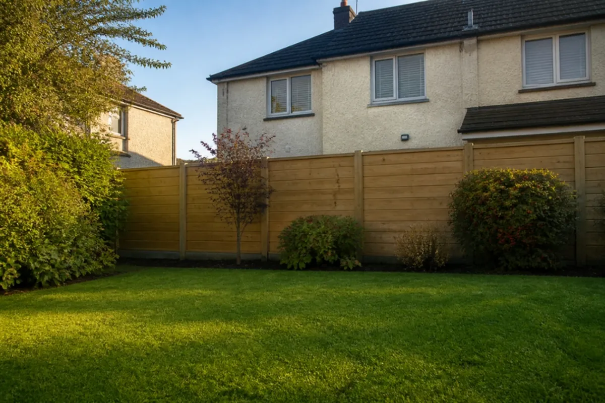 Row of new lap fence panels behind a pebbledashed semi with a lawn in front
